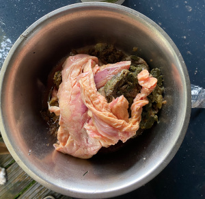 Ein Edelstahlnapf von oben photographiert. Darin verschiedene Zutaten in unterschiedlichen Texturen. Man erkennt ganz unten etwas Gemüse, darüber etwas Pansen und ganz oben Hühnerhaut mit daran hängendem Fett. Das Bild ist aus dem realen Leben, das heißt nicht appetitlich angerichtet.